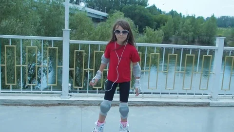 A little girl in sunglasses and headphones on rollers. Stock Footage