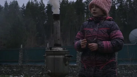 Little girl throws slivers into the fire of a smoking samovar Stock Footage 99715210