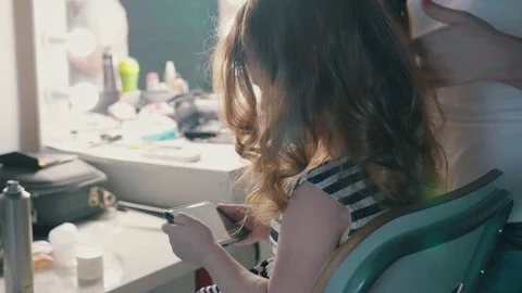 Little girl use a smartphone while sitting in a barber chair while creating a Stock Footage