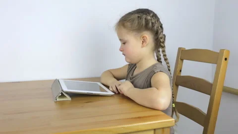 Little girl uses the tablet while sitting at the table Video stock 101385742