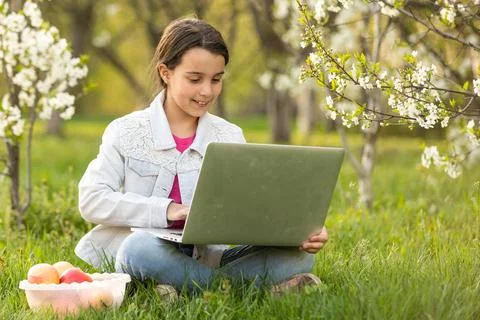 Little girl using laptop computer in a backyard. Child studying at home doing Stock Photos