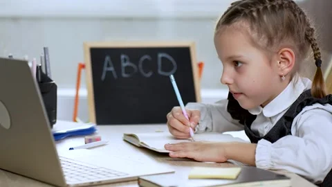 Little girl using laptop while writing notes, during online school at home Stock Footage 274292688