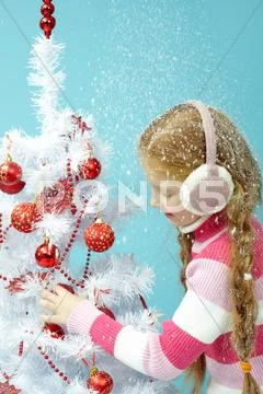 Little girl in warm clothing decorating a Christmas tree in snow Stock Photos