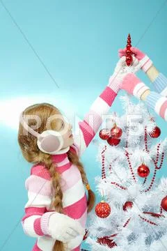 Little girl in warm clothing fixing a toy top on Christmas tree Stock Photos