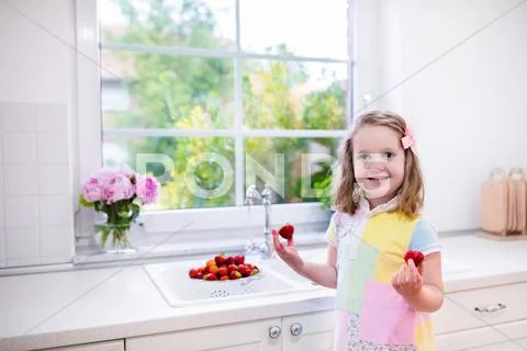 Little Girl Washing Strawberries In White Kitchen