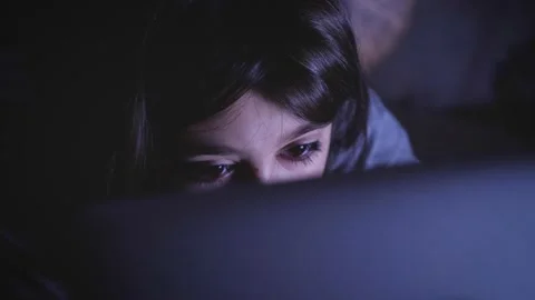 Little girl watching computer monitor in the evening. Child in the night at home Stock Footage