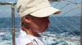 Little girl wearing cap stands on deck of ship looking ahead HD Footage