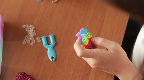 Little girl weave wristband of rubber bands. Colored rubber bands for weaving Stock Footage