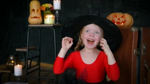 A little girl, a witch, in a hat, eats sweets and scares the camera. Stock Footage 80636453