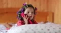 Little girl with a wreath on his head and with red smartphone lies on the bed HD Footage