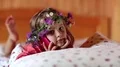 Little girl with a wreath on his head and with red smartphone lies on the bed HD Footage