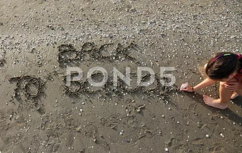 Little girl writes the phrase Back to School on the beach Stock Photos
