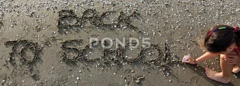 Little girl writes the phrase Back to School on the beach in summer Stock Photos