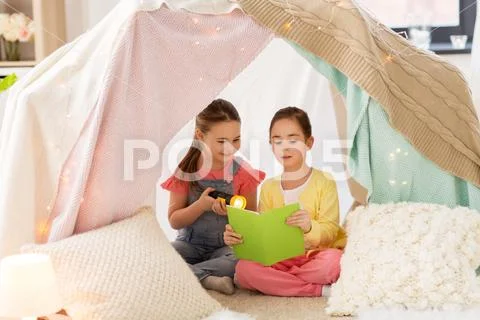 Little girls reading book in kids tent at home Stock Photos