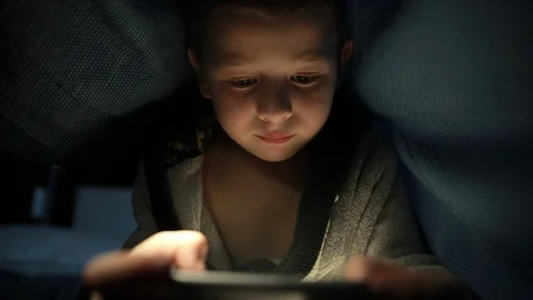 Little guy under the blanket is playing a game on his phone smartphone at night Stock-Footage 125739670