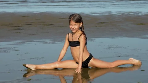 Little gymnast doing stretching exercise on a beach. Girl practicing split po Stock Footage 284845448