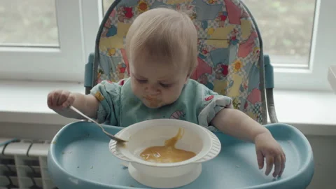 Little Kid Eats Himself Spoon Baby Food Sitting In Baby Chair At Home Stock Footage 143810435