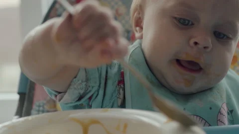 Little Kid Eats Himself Spoon Baby Food Sitting In Baby Chair At Home Stock Footage 143810907