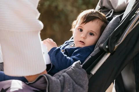 Little kid looking at camera while sitting in the stroller pram outdoors. Stock Photos