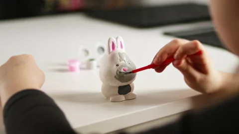 Little kid painting ceramic easter bunny figure. Child making DIY craft Stock Footage 189937616