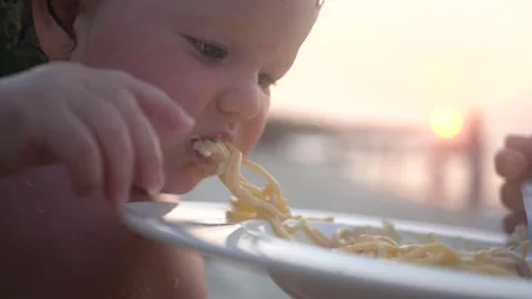 Little kid on vacation eats spaghetti with appetite at sunset by the sea. HD Stock Footage 132904874