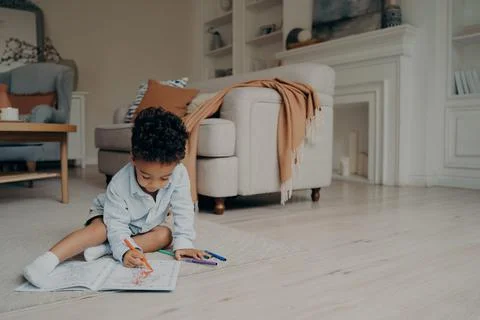 Little mixed race kid boy drawing in coloring book while spending leisure time Stock Photos