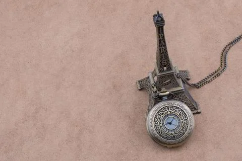 Little model Eiffel Tower and a pocket watch on brown background Stockillustratie