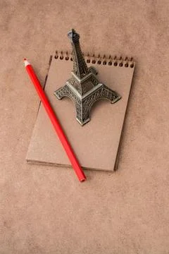 Little model Eiffel Tower notebook and a pencil on brown background Ilustración de archivo