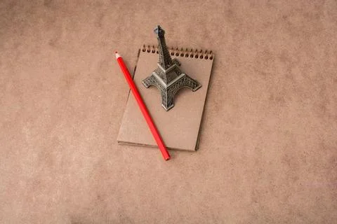 Little model Eiffel Tower notebook and a pencil on brown background Ilustración de archivo