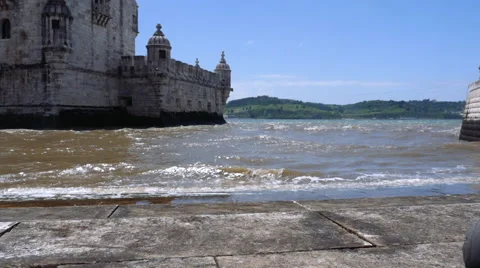 Little ocean waves hitting shore near old tower with boat and mountains 库存影片 65029099