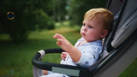 Little one seated in stroller gazes at floating bubbles Stock Footage 340885951