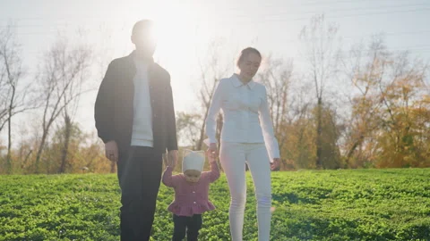 Little one takes initial outdoor steps with parental support nearby. Parents 库存影片 331532520