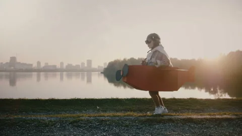Little pilot boy starting to run in fun cardboard plane at sunset backlight city Stock Footage 99772765