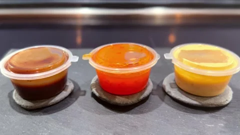 Little plastic pots of condiments brown red and yellow sauce food toppings Vidéo 345847600