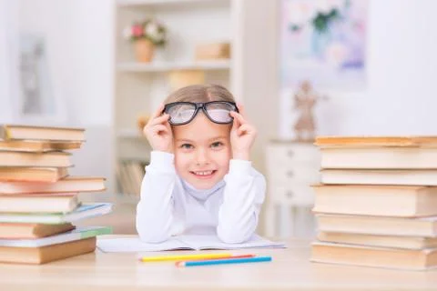 Little positive girl is at the desk with many books 库存照片