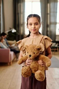 Little pretty girl with soft brown teddybear looking at you against her family Stock Photos