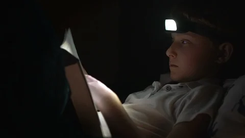 Little reader boy turns book page, he uses the Head Torch for a book reading in  Stock-Footage 105559736