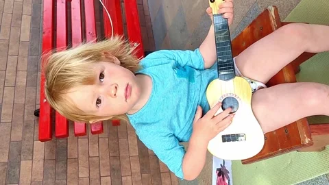 A little red-haired boy sits on the street and plays a small guitar. Stock Footage 226732509