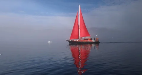 Little red sailboat among Greenlandish icebergs. Stock Footage