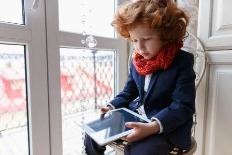 Little redhead boy uses a tablet PC sitting in his room at home Stock-Fotos