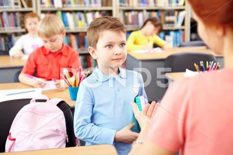 A little schoolboy communicating with a teacher in classroom Stock Photos
