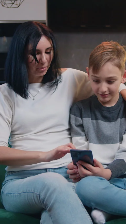 Little schoolboy siting with mom on sofa use smartphone in modern kitchen. Mothe Stock Footage 330060733