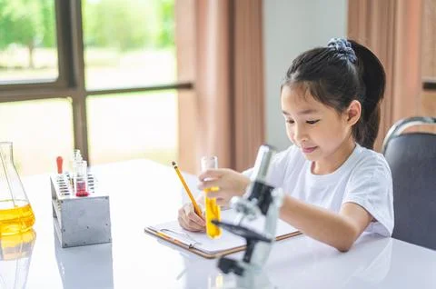 Little scientist looking through a microscope and test tubes filled with ch.. Stock Photos