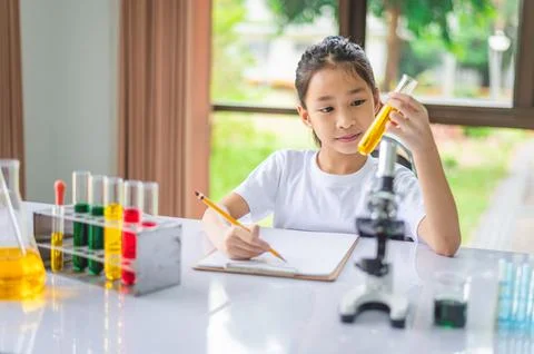 Little scientist looking through a microscope and test tubes filled with ch.. Stock Photos