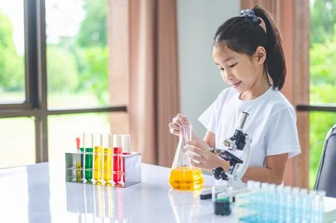 Little scientist looking through a microscope and test tubes filled with ch.. Stock Photos