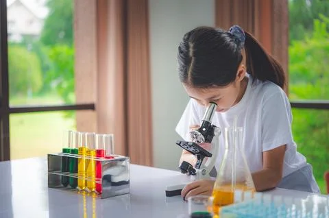 Little scientist looking through a microscope and test tubes filled with ch.. Stock Photos