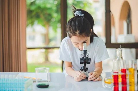 Little scientist looking through a microscope and test tubes filled with ch.. Stock Photos