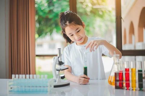 Little scientist looking through a microscope and test tubes filled with ch.. Stock Photos