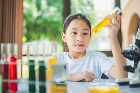 Little scientist looking through a microscope and test tubes filled with ch.. Stock Photos