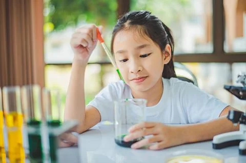 Little scientist looking through a microscope and test tubes filled with ch.. Stock Photos